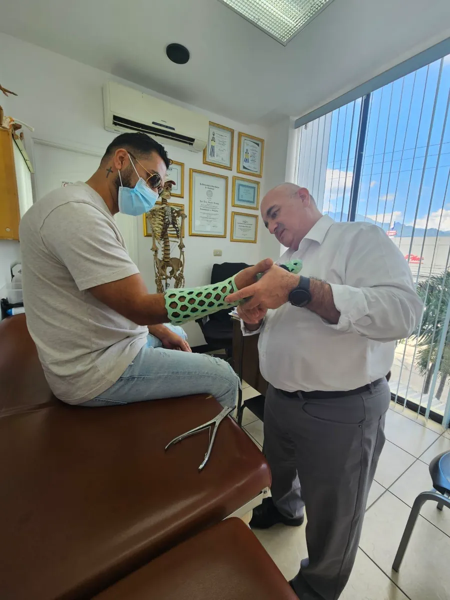 A clinician fitting a green FlexiOH short arm immobilizer to a seated patient
