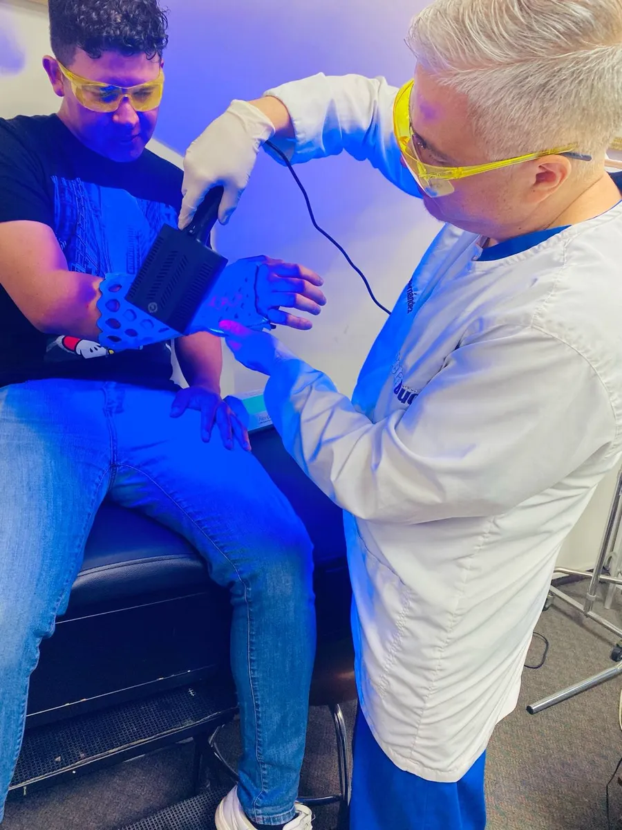A clinician curing a FlexiOH forearm immobilizer with the RizyCure light, both wearing goggles