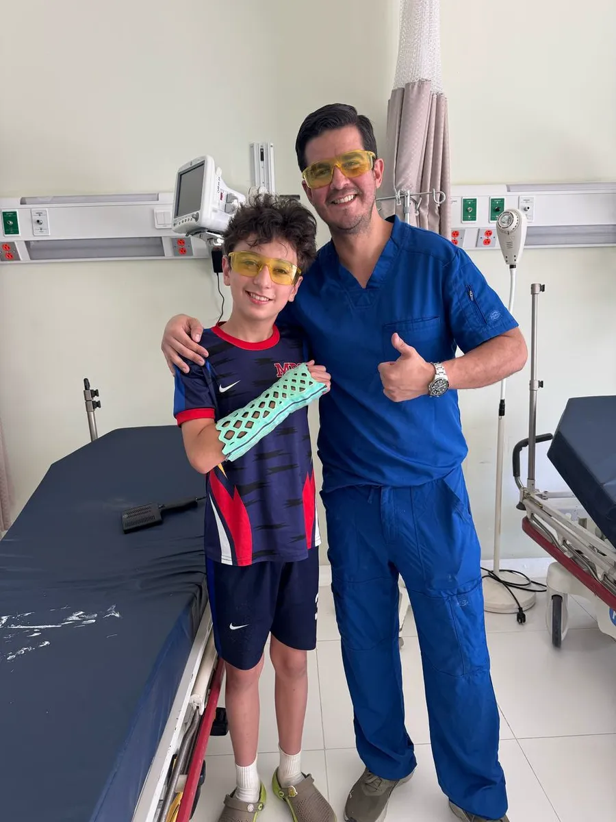 A boy holding up his cured green FlexiOH short arm immobilizer beside his clinician