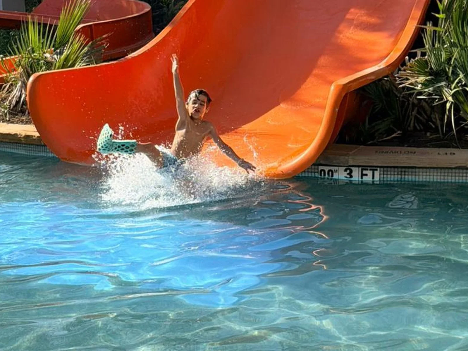 A boy landing in a waterpark pool wearing a green FlexiOH short leg immobilizer